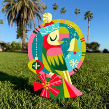Colorful Jingle Christmas metal yard stake featuring a festive parrot design against a sunny outdoor backdrop.